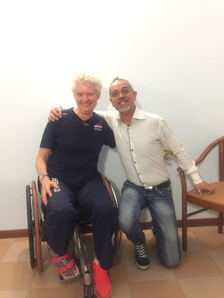 Un'immagine che ritrae sedia a rotelle, seduta, sorriso, gomito e ginocchio.